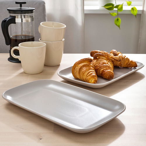 Mesa con tres croissants en plato rectangular, dos tazas apiladas y una prensa de café.