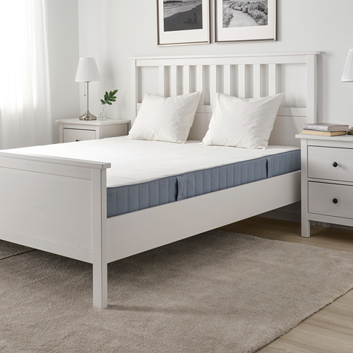 Dormitorio minimalista blanco con colchón VESTMARKA, mesas auxiliares, lámpara, planta, arte, alfombra.