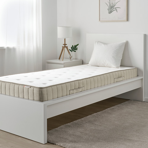Dormitorio minimalista con colchón blanco, mesita de noche, lámpara y planta.