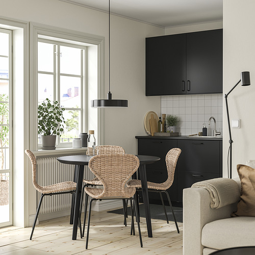 Cocina moderna con mesa negra LISABO y sillas naturales, ventana, armarios negros, sofá crema.