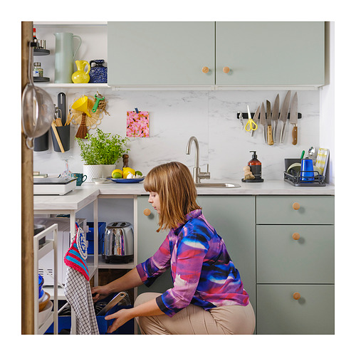 Cocina moderna con gabinetes beige, encimeras de mármol. Mujer lavando platos, hierbas y herramientas.