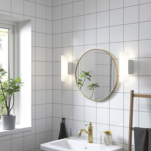 Baño moderno con espejo dorado, lavamanos, luces, planta y toallas.