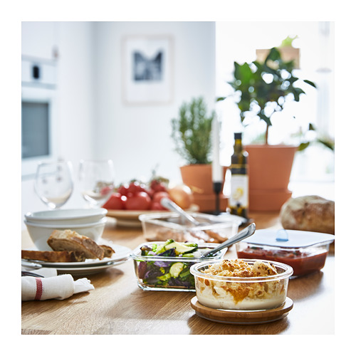 Recipientes de vidrio para alimentos IKEA 365+, transparentes, redondos, llenos de comidas variadas, colocados sobre mesa de madera, ideales para almacenar y calentar alimentos.