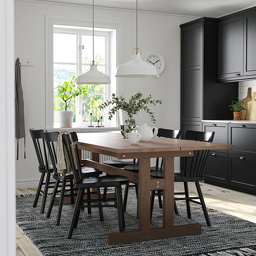Cocina moderna con mesa y sillas KLIMPFJÄLL negras, suelo de madera, armarios negros, lámparas colgantes blancas, plantas verdes y un reloj blanco.