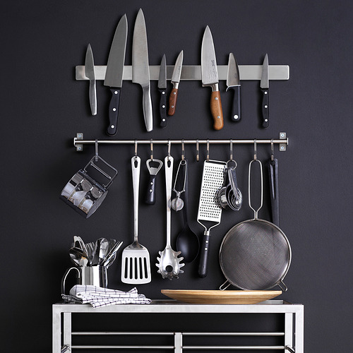 Almacenamiento de cocina montado en la pared con cuchillos, utensilios y soporte sobre fondo oscuro.