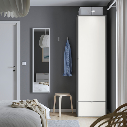 Dormitorio moderno y minimalista con armario alto VISTHUS blanco, toalla azul, taburete pequeño, espejo grande, cama blanca, paredes grises.
