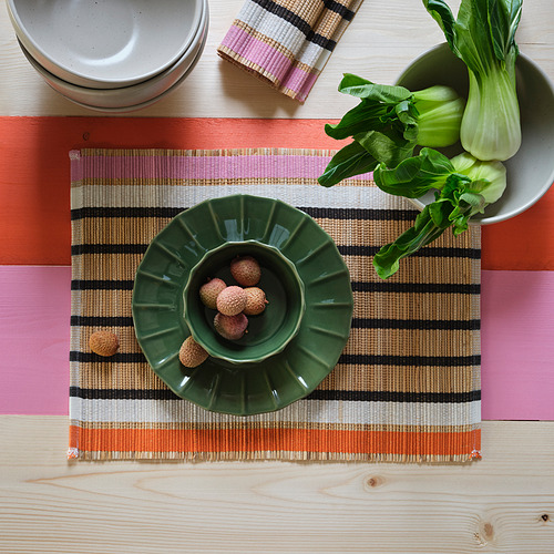 Mesa con tapete tejido, cuenco verde de lichis y bok choy en una bandeja.