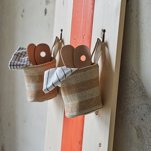 La cesta de yute MÄVINN cuelga con cucharas de madera sobre tablas rojas y blancas.