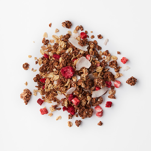 Mezcla de granola colmada con avena crujiente de chocolate, hojuelas de coco y bayas secas de color rojo brillante sobre una superficie blanca.