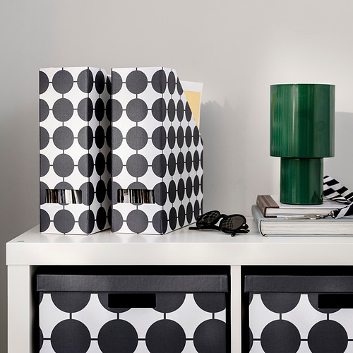 Revistero TJENA de lunares en blanco y negro sobre escritorio con lámpara y libros.