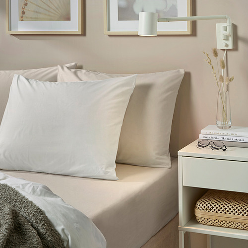 Sábana bajera DVALA beige y almohadas grandes en la cama. Mesita de noche con jarrón, libros, gafas. Minimalista y relajante.