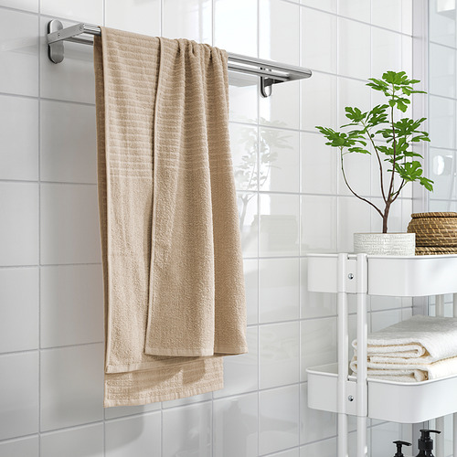 Toallas VÅGSJÖN beige en estante, estante con planta y cesta, paredes de azulejos limpios.