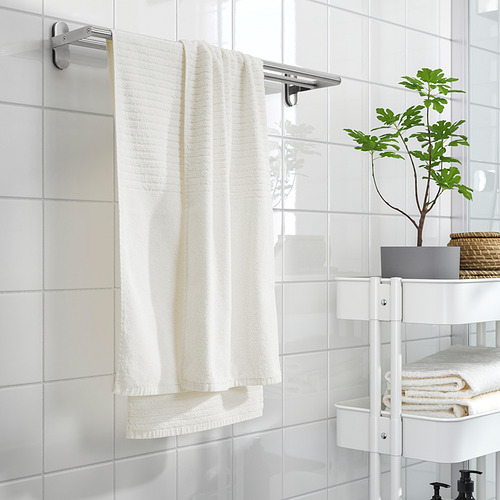 Toallas VÅGSJÖN blancas sobre barra cromada en baño minimalista con carrito.