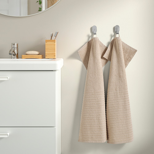 Las toallas VÅGSJÖN beige cuelgan de ganchos junto al armario blanco del baño.