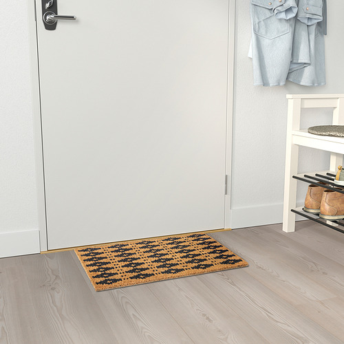 Un felpudo de rayas marrones y negras se encuentra en el interior de una puerta, capturando eficazmente la suciedad y conectándose a un zapatero, mejorando la limpieza de la entrada.