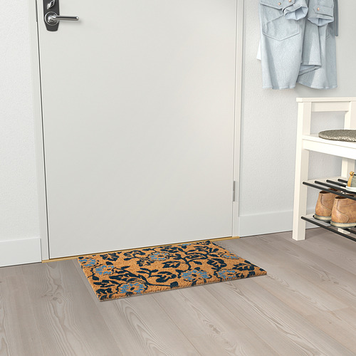 El felpudo floral azul cerca de la puerta blanca y el zapatero atrapa la suciedad.