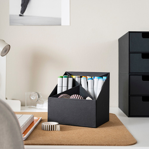 Escritorio de oficina con organizador que sostiene rotuladores y bolígrafos, junto a un rollo de cinta adhesiva sobre una estera de corcho, junto a una pila de cajones.