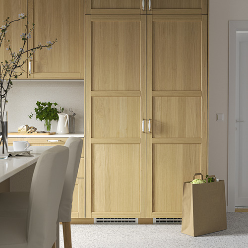 Cocina moderna con nevera, silla, jarrón, tetera y comestibles FORSNÄS de madera clara.