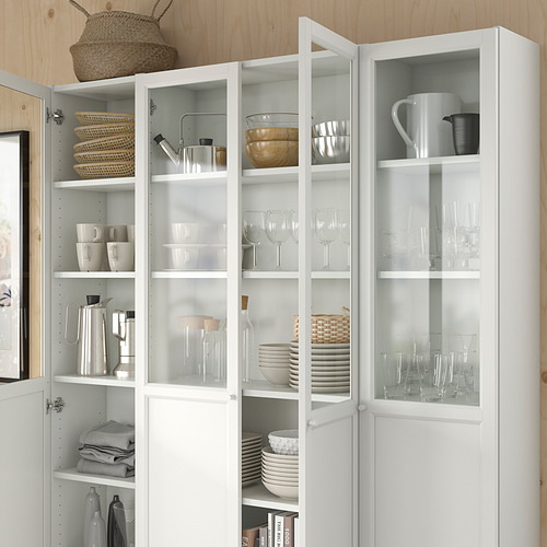 Mueble OXBERG blanco con puertas de cristal que exhiben platos, vasos y cesta.