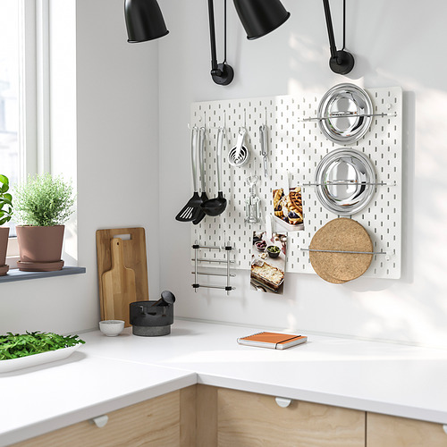 Cocina blanca con tablero perforado SKÅDIS, utensilios y especias. Almacenamiento eficiente y ajustable junto a armarios y plantas.
