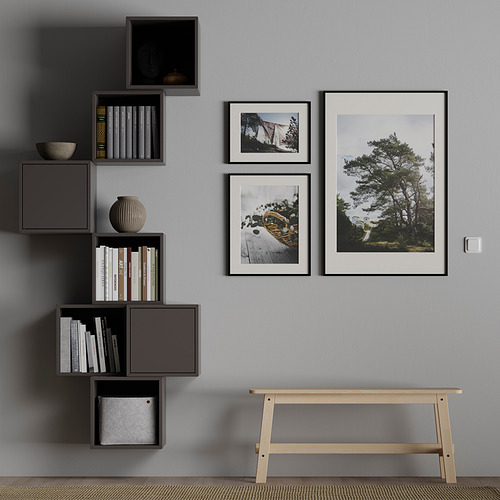 Sala moderna con estanterías modulares de pared gris que sostienen libros blancos y negros. Fotos de la naturaleza enmarcadas y un banco de madera.