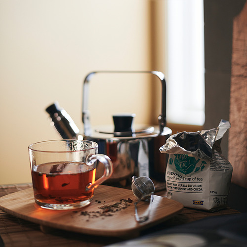 Taza de vidrio transparente en bandeja de madera, con tetera plateada y bolsita de té, que muestra la facilidad de ver la fuerza del té.