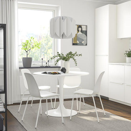 Comedor moderno con mesa DOCKSTA blanca, cuatro sillas, base de metal, lámpara colgante, plantas y cuadro en una habitación minimalista.