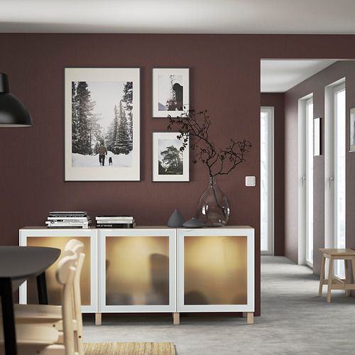 Aparador blanco BESTÅ con puerta de cristal y estantes abiertos contra la pared oscura.