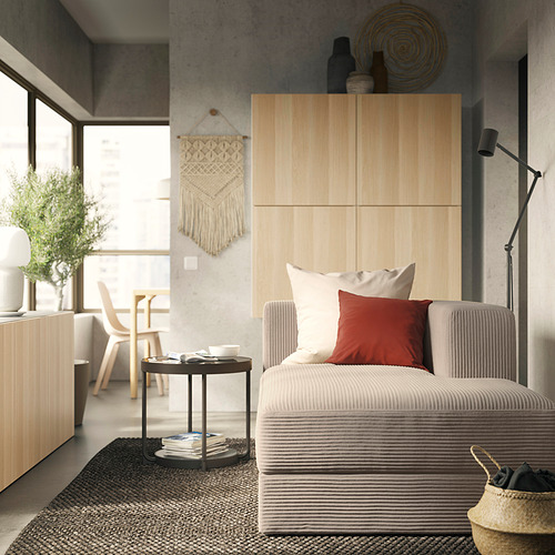 Salón moderno con sofá JÄTTEBO, tonos neutros, acentos rojos, libros, lámpara de pie, macramé, plantas.