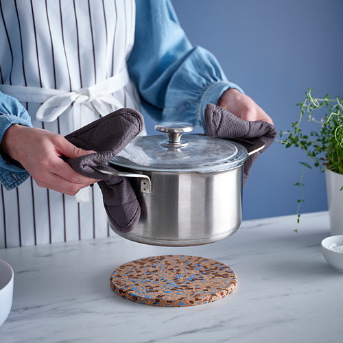 Las manos con guantes colocan la tapa en el salvamanteles. Puntos azules en el corcho de la cocina.