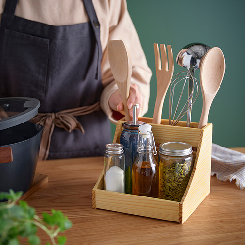 Representa a una persona preparando alimentos con un portautensilios de madera que contiene varios utensilios de cocina de madera y frascos de condimentos.