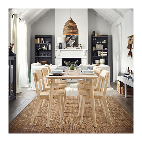 Comedor natural con mesa de madera clara, sillas y una alfombra tejida; sofá de felpa y cálida lámpara colgante.