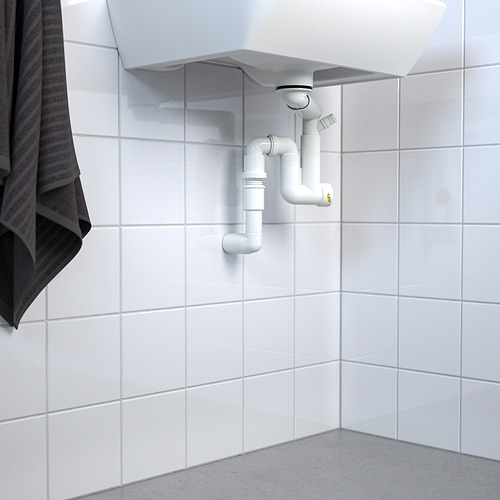 Fregadero blanco con trampa de agua RÄNNILEN visible y tubería flexible contra la pared de azulejos.