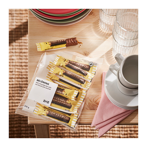 Tabletas de chocolate con la etiqueta BELÖNING, envueltas y sin envolver, con platos y tazas sobre una mesa de madera.