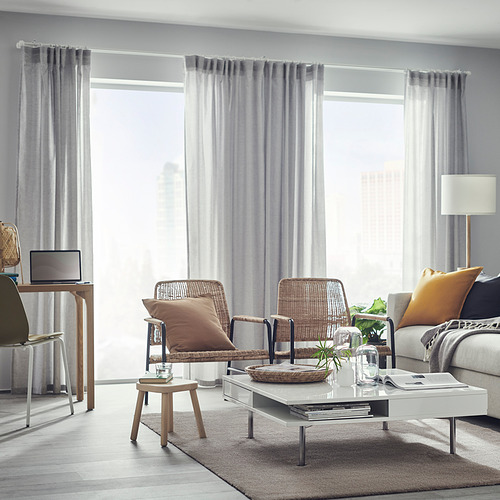 Sala de estar moderna con alfombra gris, sillas de mimbre y mesa de centro de vidrio junto a grandes ventanales.