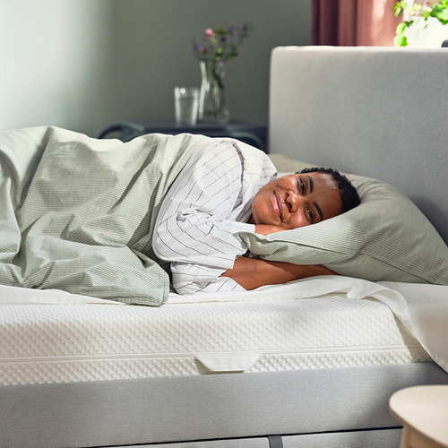 Una persona durmiendo plácidamente en un colchón blanco ÅBYGDA, cubierto con una manta de color claro.