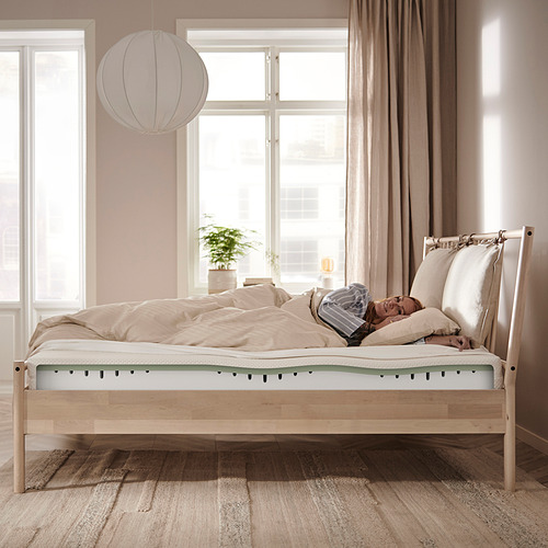 Colchón de espuma beige con memory top, sobre cama de madera en habitación luminosa.