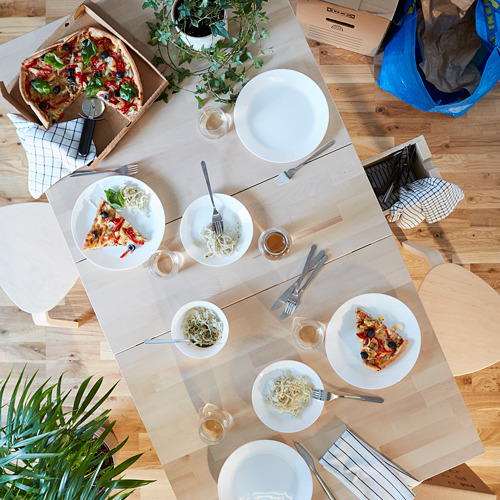 Vista superior de una mesa rústica con un juego de vajilla de madera OFTAST que incluye platos, cuencos y cubiertos. También se ve una caja de pizza, vasos y una bolsa azul.