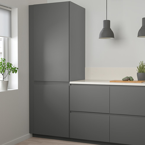Cocina moderna con armarios altos VOXTORP de color gris oscuro, diseño elegante, manijas integradas y plantas en macetas.