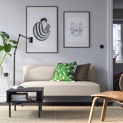 Sala de estar moderna con sofá beige, almohadas verdes, arte, lámpara lateral, libros, taza de café, alfombra, planta.