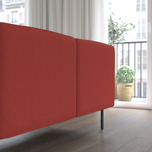 Sofá LILLEHEM rojo brillante con un gran cojín de asiento y respaldo, colocado cerca de una gran ventana que ofrece una vista de la ciudad.