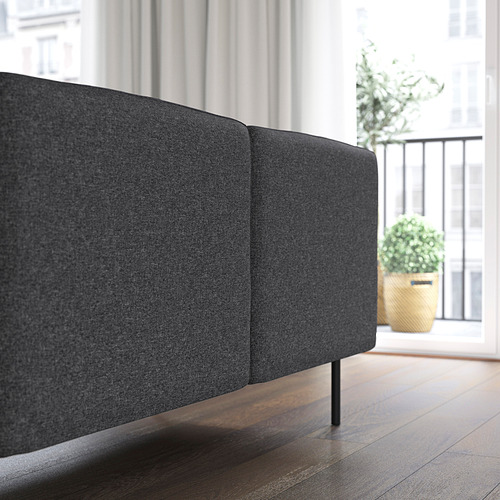 Sección de sofá modular gris oscuro con patas robustas cerca de una gran ventana.