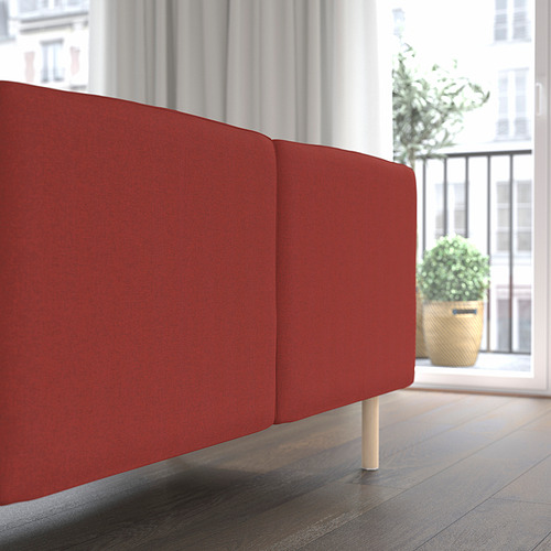 Sofá modular rojo, cojines de respaldo y asiento a la vista, colocados cerca de una ventana con plantas.