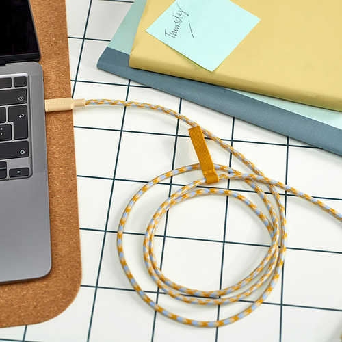 Un espacio de trabajo con una computadora portátil, un cuaderno, una nota adhesiva y un cable usb-c de carga rápida amarillo y azul en espiral con banda elástica adjunta para la organización.