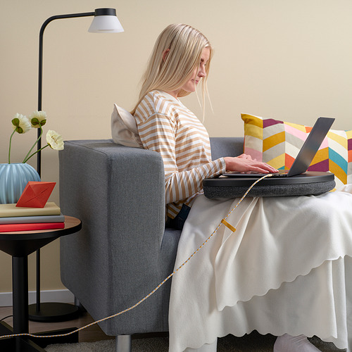 Mujer con camisa a rayas trabaja en la computadora portátil en la mesa con lámpara y flores.