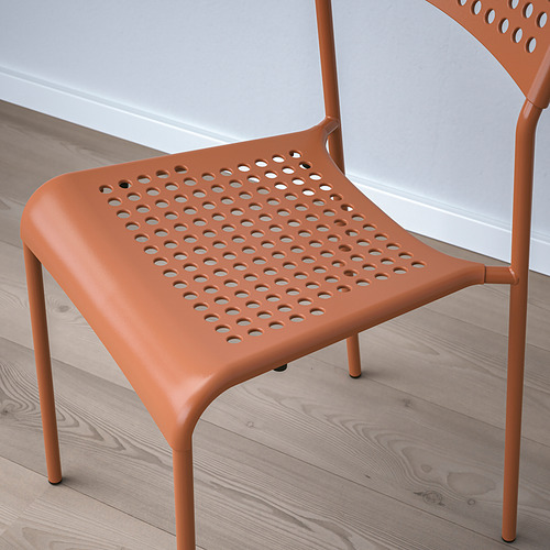 Silla moderna de color naranja brillante con asiento y respaldo perforados, colocada sobre suelo de madera. Construcción de plástico y metal de alta calidad.