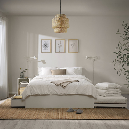 Dormitorio minimalista con cama VIHALS blanca, suelo de madera clara, alfombra beige, zapatillas grises, almohadas blancas y luz colgante. Tres fotos enmarcadas sobre la cama.