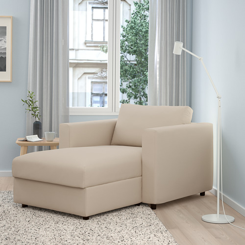 Chaise lounge VIMLE beige, con respaldo contra la pared, junto a una lámpara blanca alta, una pequeña mesa de madera y una gran ventana.