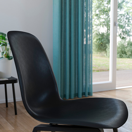Silla negra moderna con diseño elegante, colocada cerca de una ventana con cortinas turquesas y una planta.
