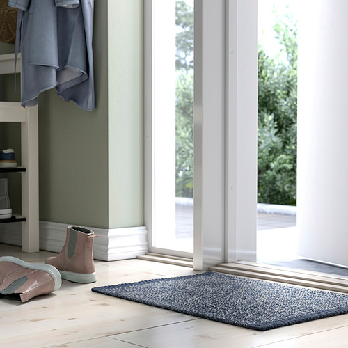 Estera tejida azul cerca de botas rosas, debajo de un abrigo gris colgante.